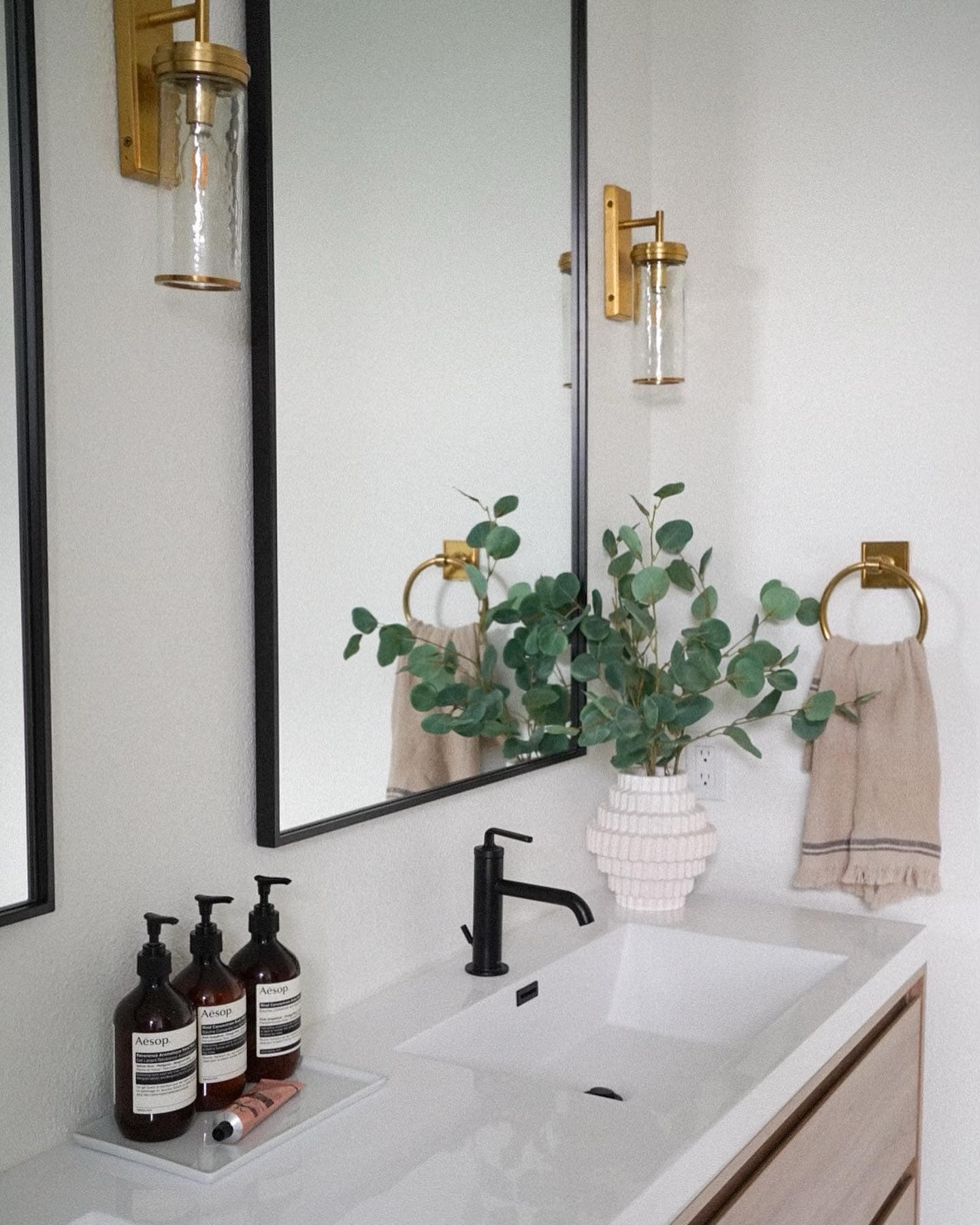 Bathroom vanity detail with a black faucet, brass sconce, and eucalyptus in a Highlands Ranch home