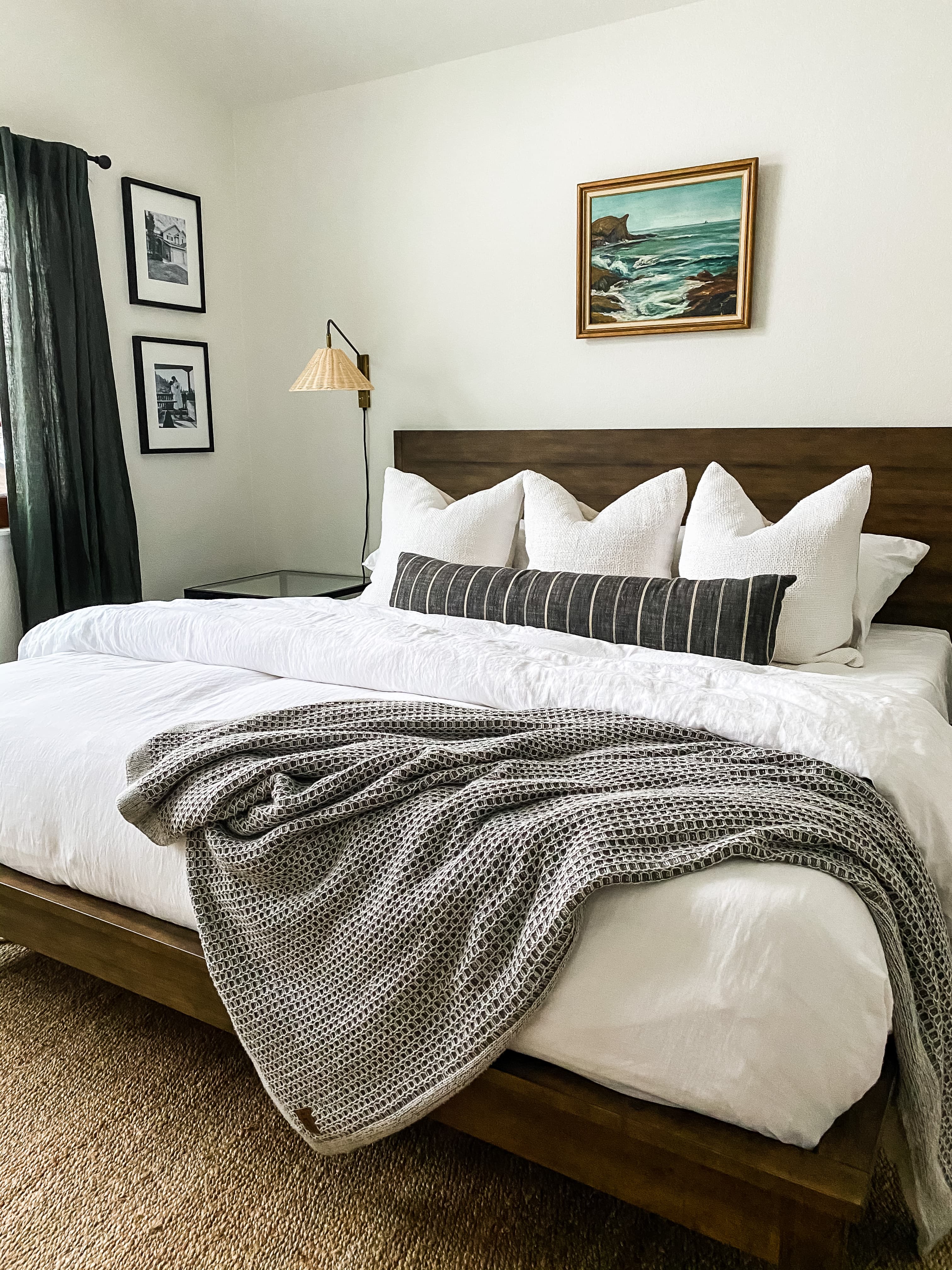Highlands Ranch bedroom with a wood platform bed, white bedding, a vintage seascape painting, and a rattan wall sconce