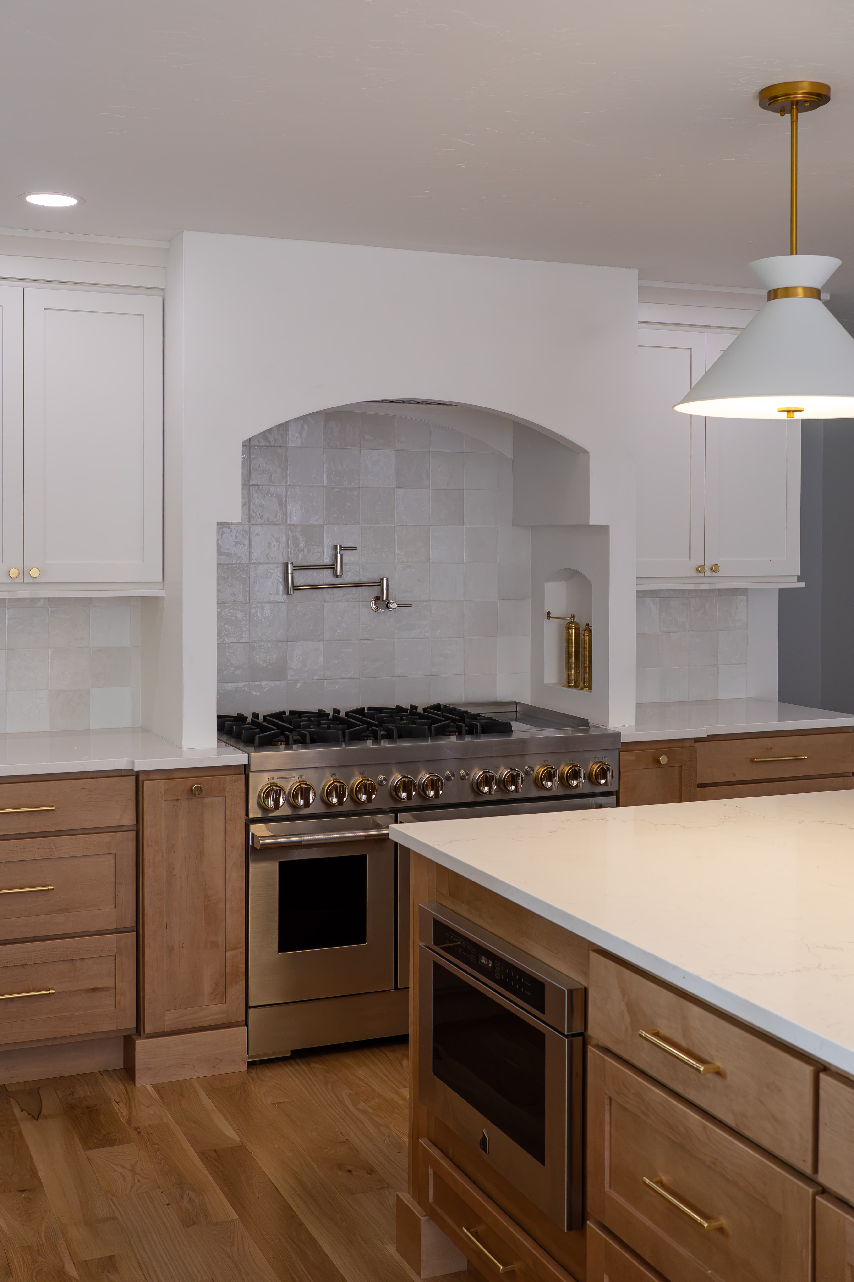 Range wall with zellige-look tile, soft white uppers, and a maple island with brass pulls in a Greenwood Village kitchen