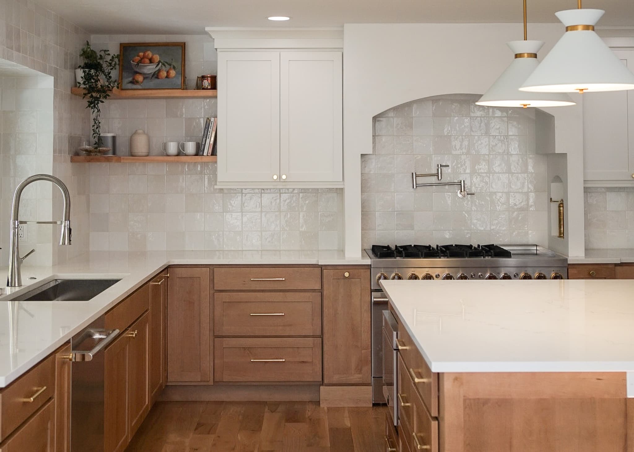 Two-toned kitchen in Greenwood Village with honey maple lower cabinets, soft white uppers, a custom arched range hood, and white pendants, designed by Halcyon Haus