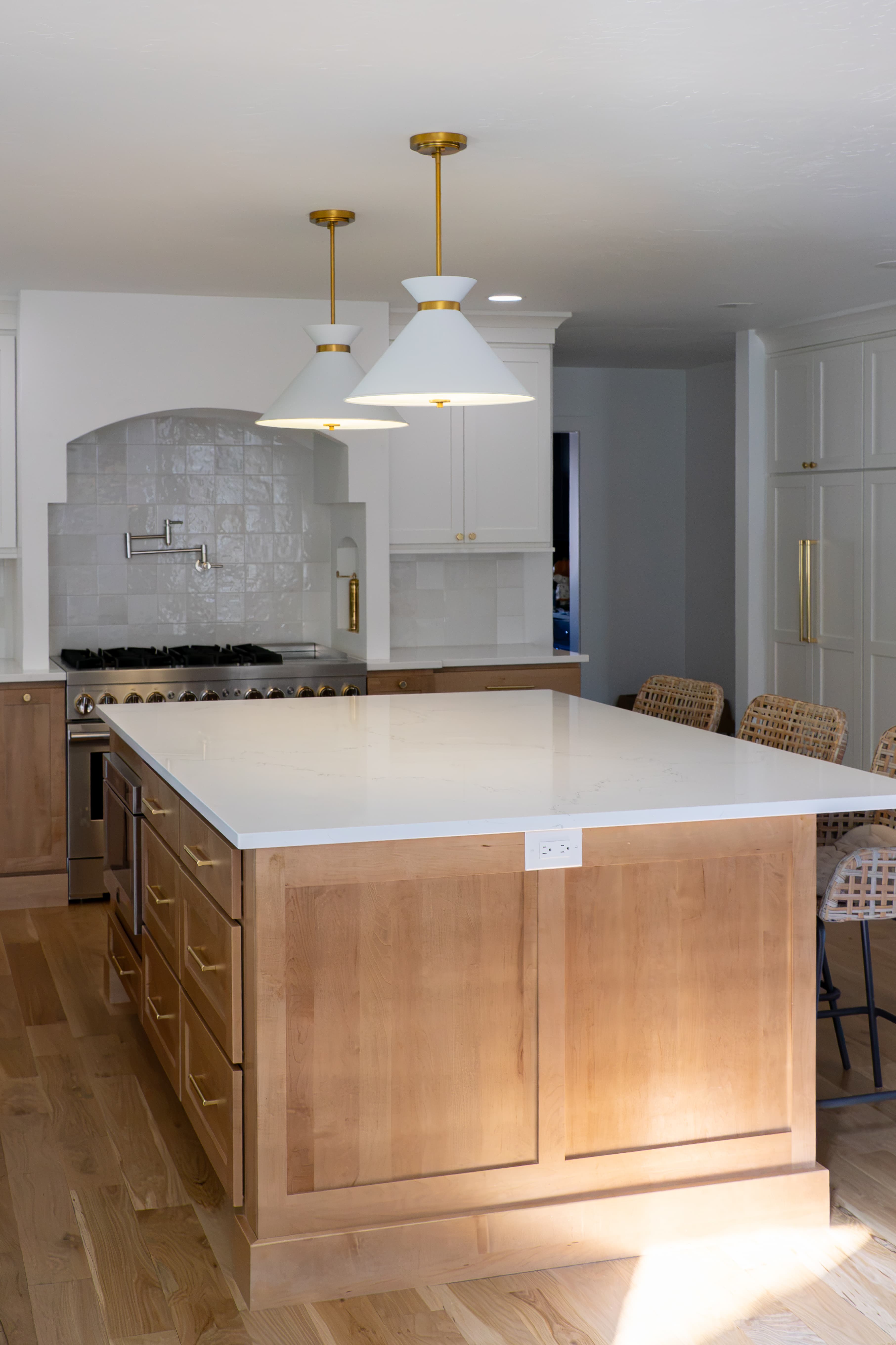Large honey maple island with quartz countertop, white pendants, and woven counter stools in a Greenwood Village kitchen