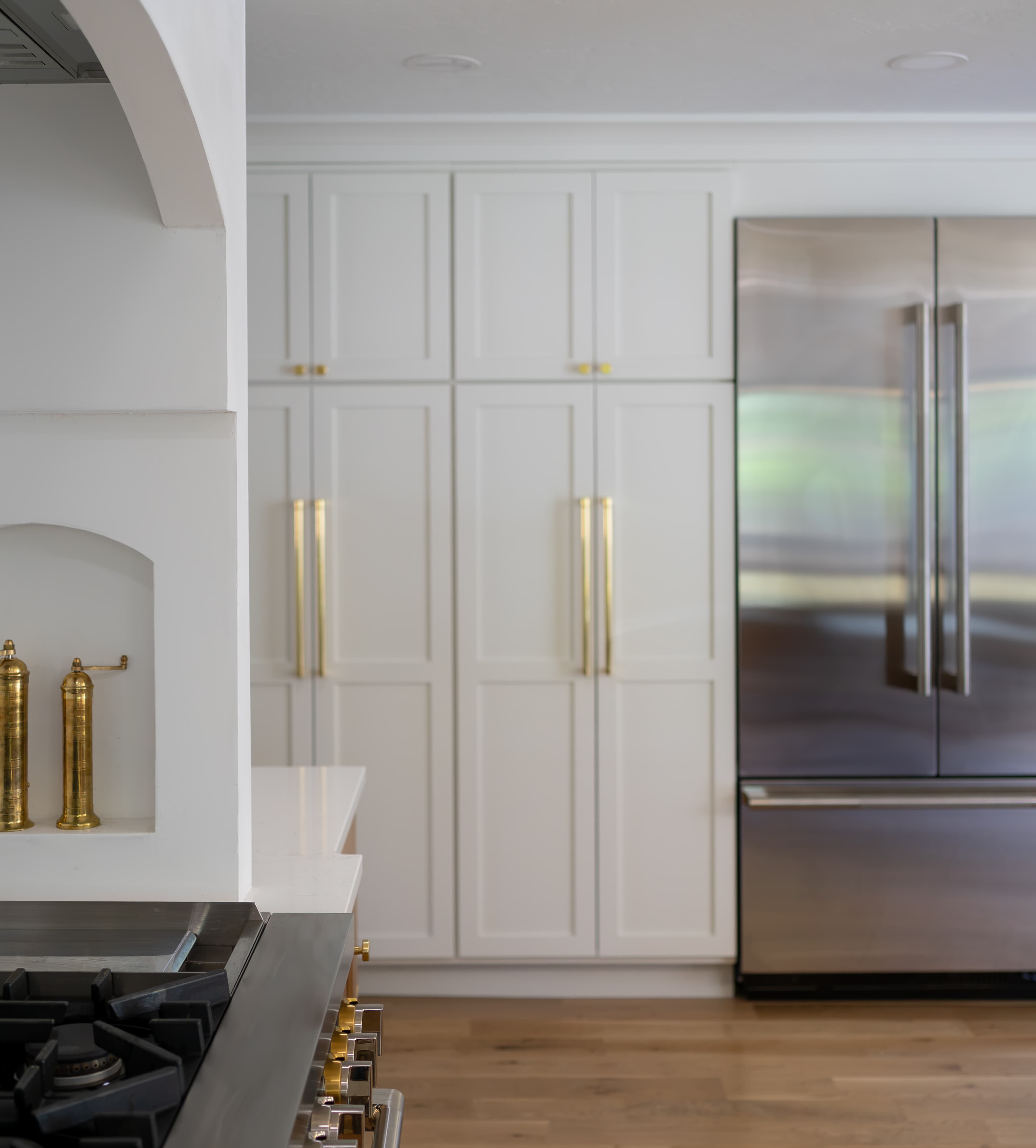 Floor-to-ceiling soft white pantry cabinets with long lacquered brass pulls beside the refrigerator in a Greenwood Village kitchen