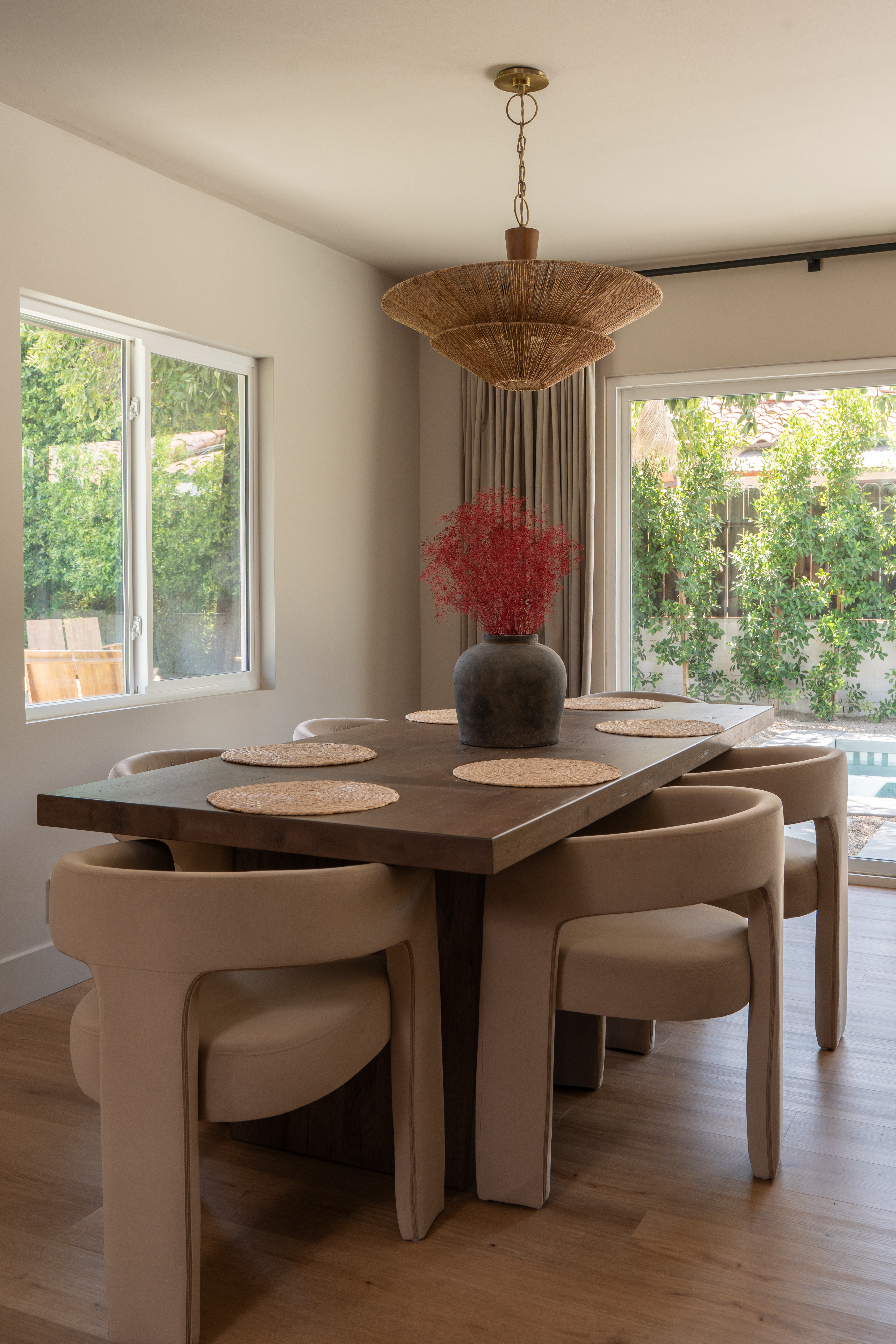 Dining room with dark wood table, sculptural upholstered chairs, and a tiered woven pendant, with glass doors open to the pool in Palm Springs home