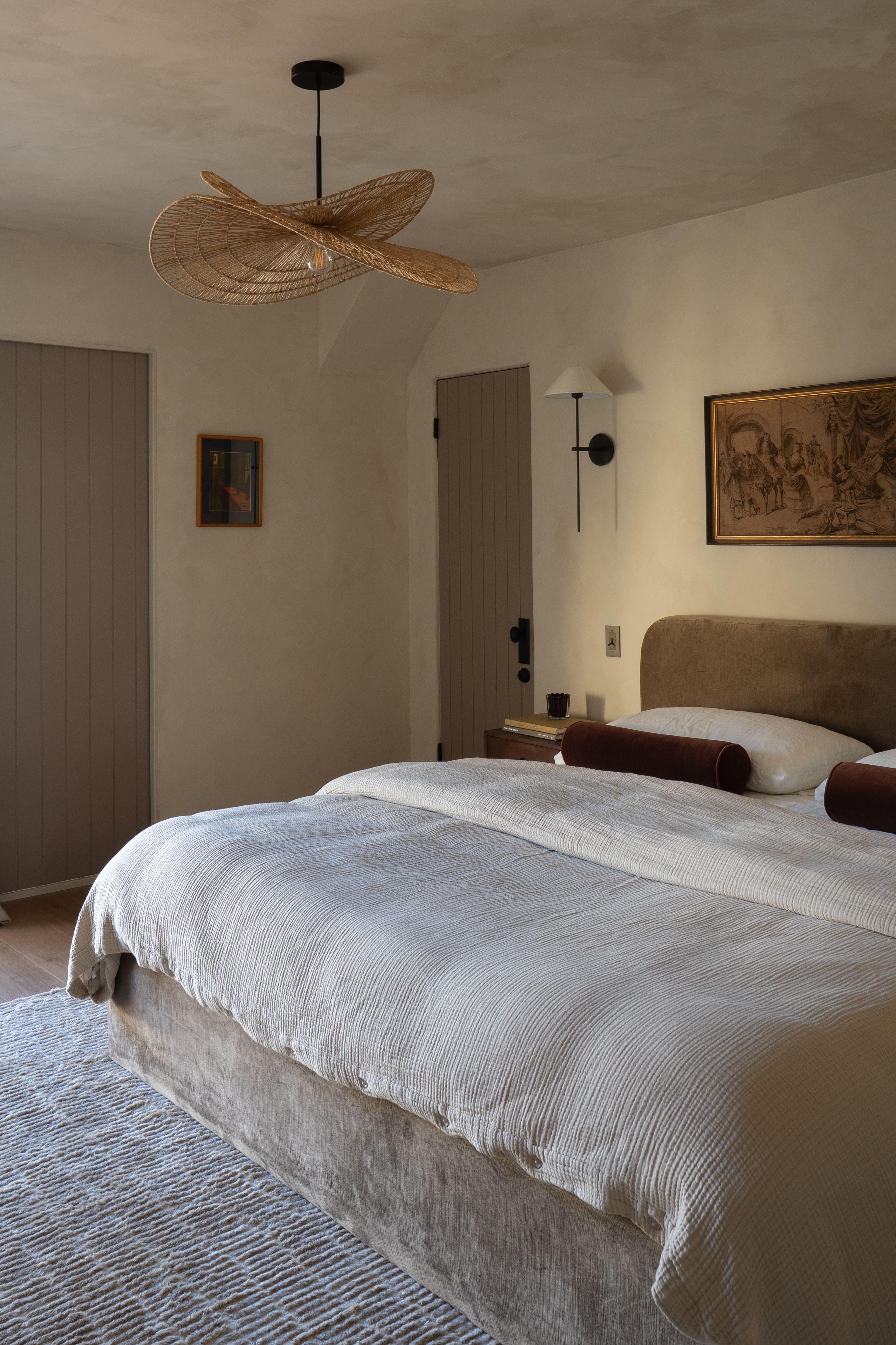 Primary bedroom with plaster walls, woven pendant light, and burgundy velvet bolster pillows in Palm Springs home