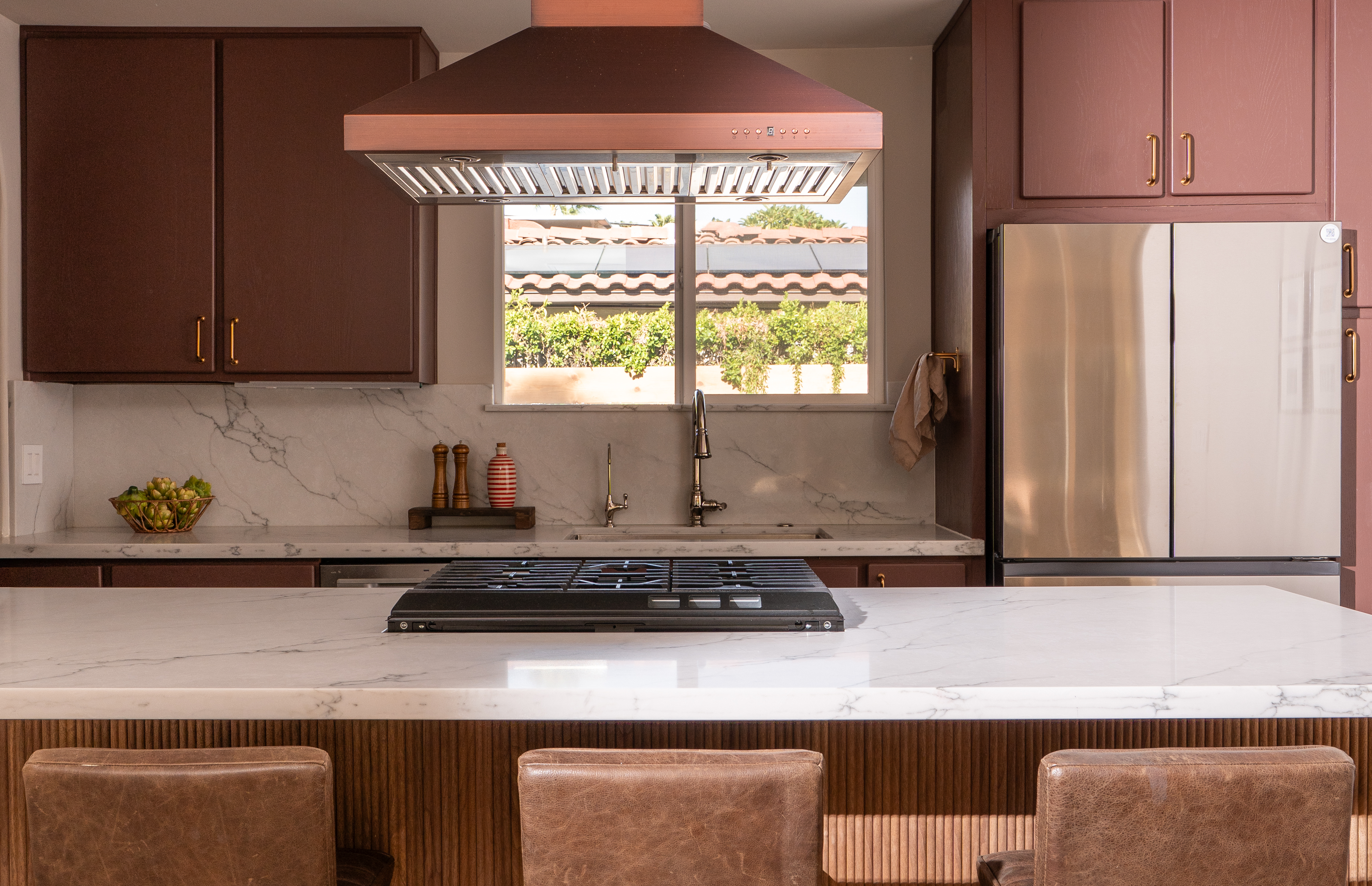 Palm Springs kitchen with burgundy cabinetry, copper hood, and fluted wood island, designed by Halcyon Haus