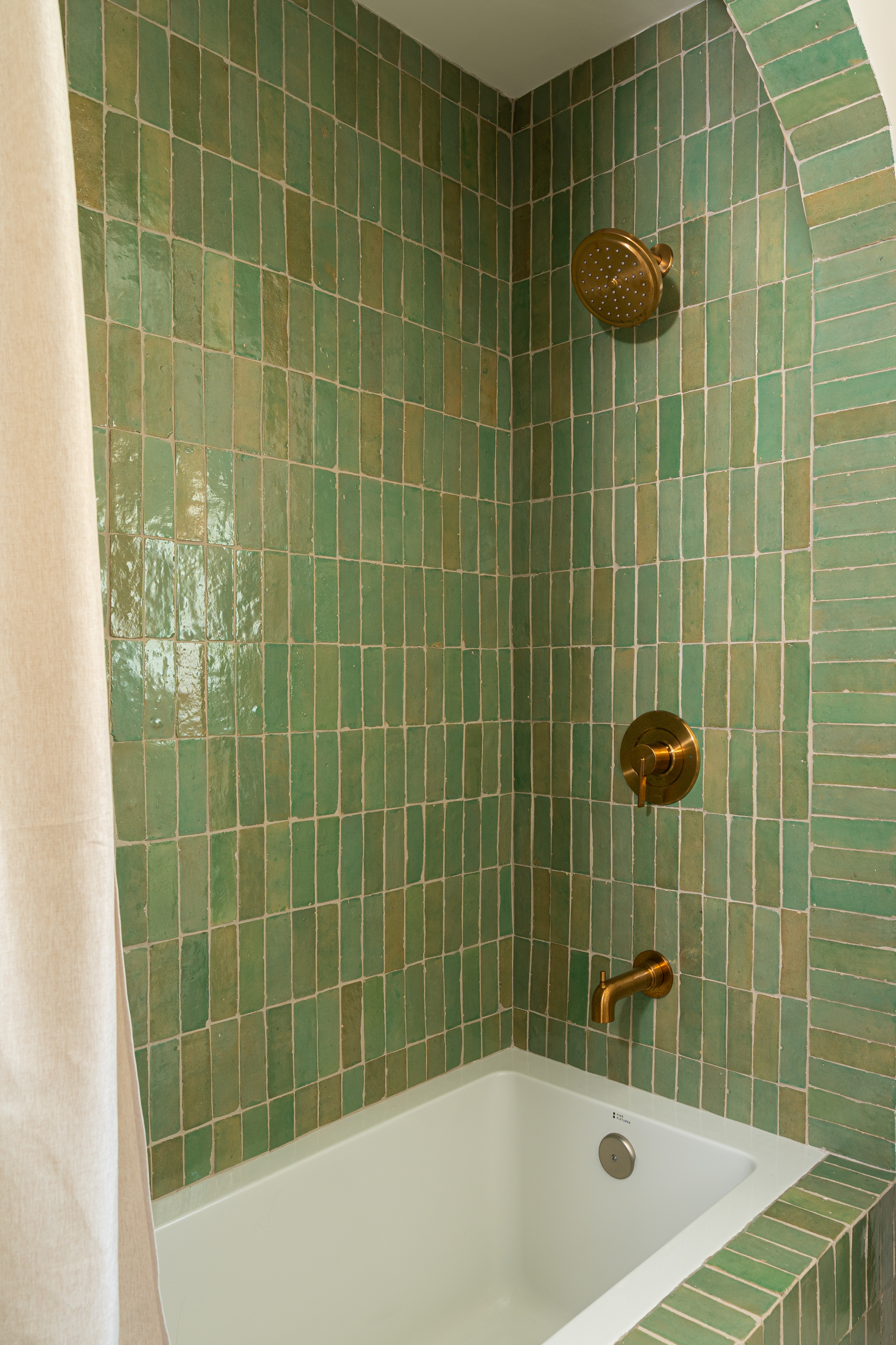 Tub surround in green zellige tile with an arched edge and brass shower fixtures in Palm Springs bathroom