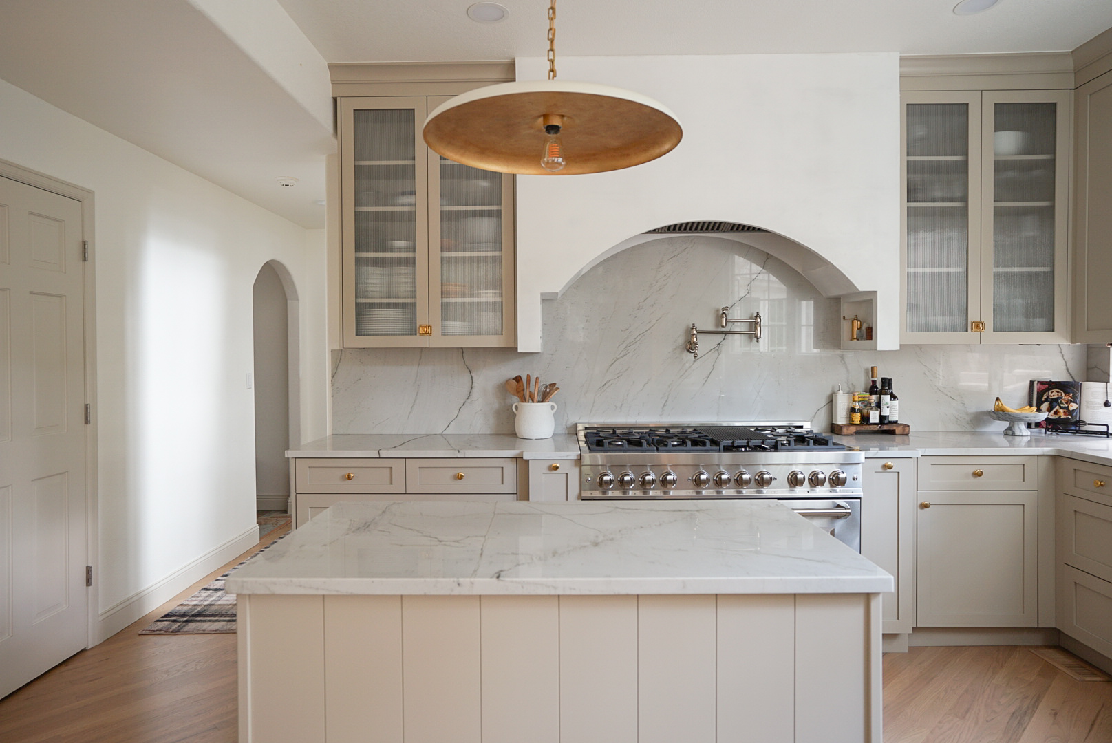 Full kitchen view showing layered metal finishes and natural stone backsplash