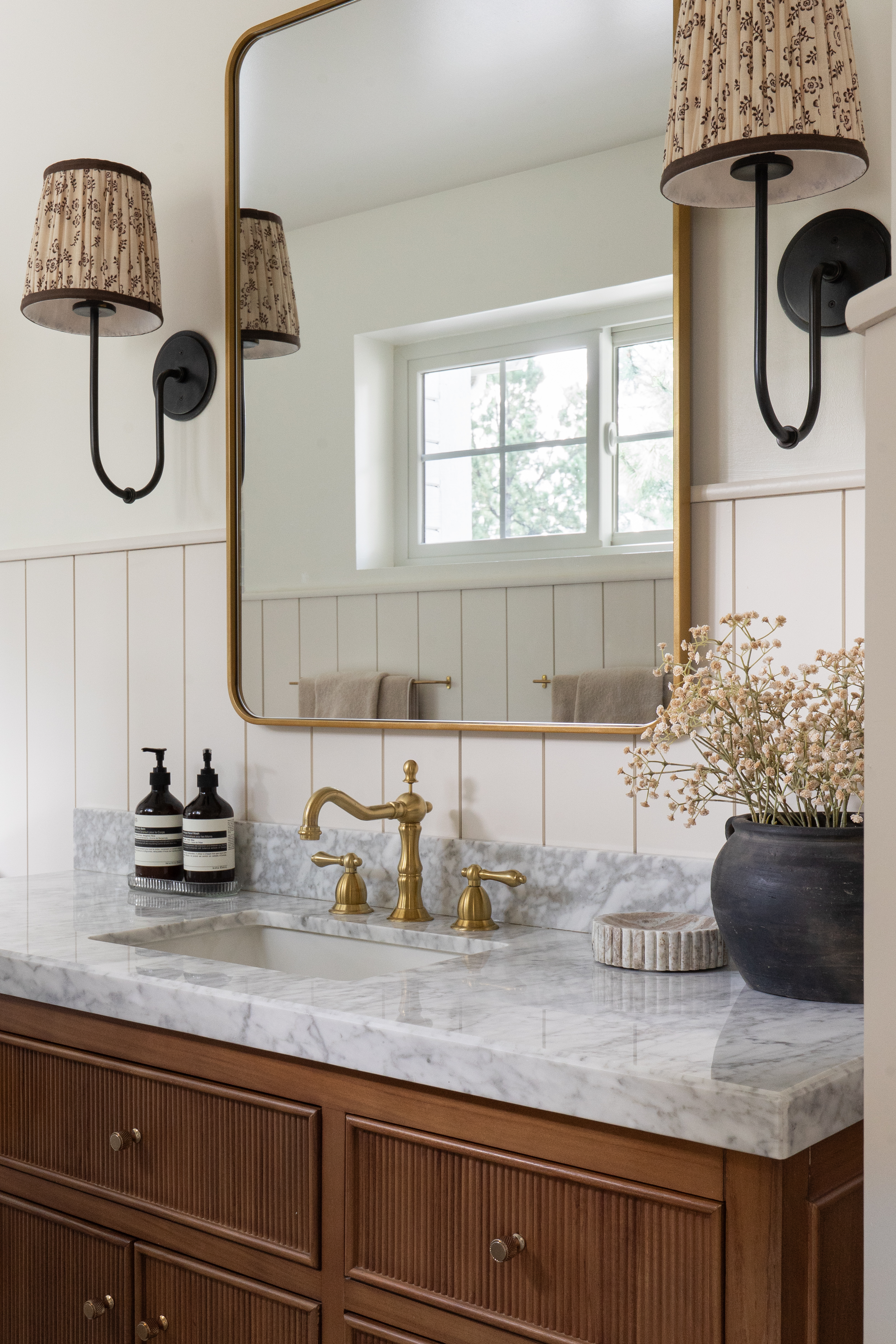 Single vanity detail with brass mirror, pleated sconces, and marble counter in Castle Pines primary bathroom